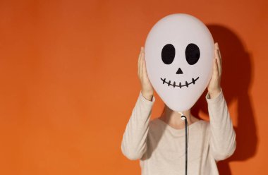 Yüzünü turuncu balonun yanına saklayan bir kadın.