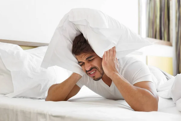 Triste hombre en la cama cabeza cubierta con almohada —  Fotos de Stock