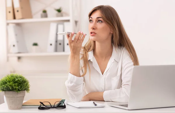 Empresária usando o assistente de voz de celular trabalhando no escritório moderno — Fotografia de Stock