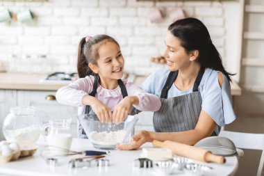 Neşeli kız ve anne önlükleriyle mutfakta birlikte yemek pişiriyor.