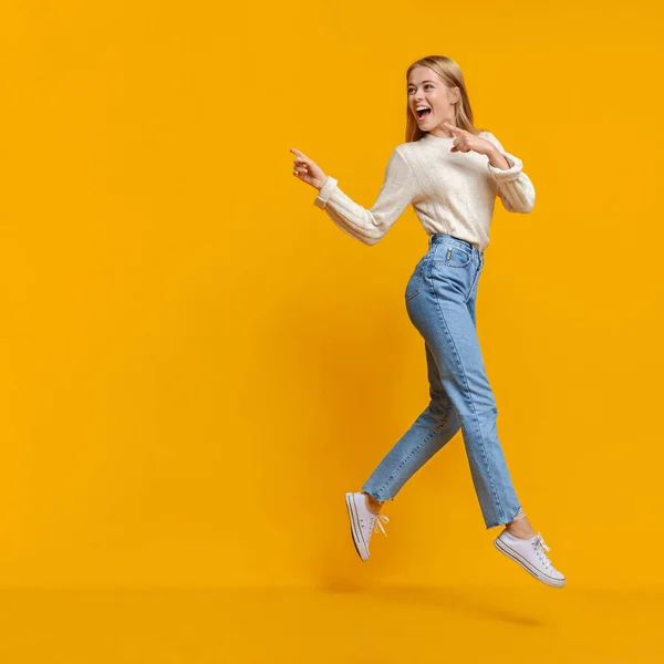 Молодая девушка прыгает в воздух и указывает на пространство для копирования — стоковое фото