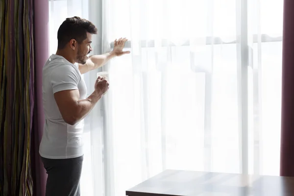 Joven que se queda al lado de la ventana, bebiendo café de la mañana —  Fotos de Stock