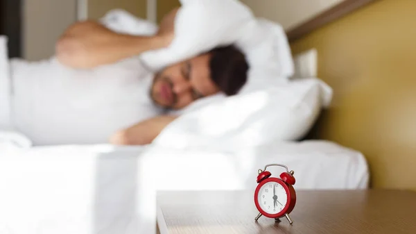 Exhausted man being awaken by alarm clock in his bedroom — Stock Photo, Image