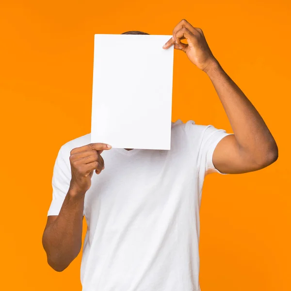 Černoch zakrývající tvář s papírovým listem stojící, oranžové pozadí — Stock fotografie