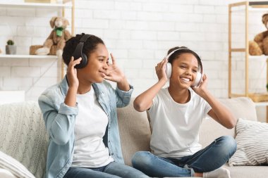 Liseli kızlar kablosuz kulaklıklarla müzik dinleyip dans ediyorlar.