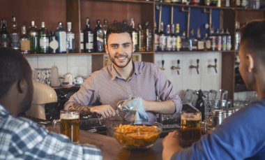 Çekici genç barmen bardakları parlatıyor, müşterilerle konuşuyor.
