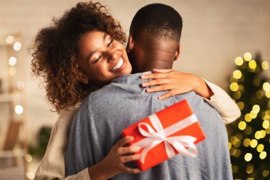 Minnettar afro kadın Noel hediyesi ile evde kocasına sarılıyor.
