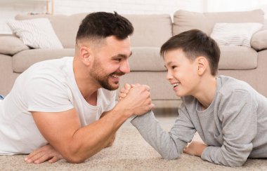 Baba oğul bilek güreşi yapıyor, evde yerde yatıyor.