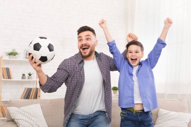 Duygusal baba ve oğul futbol topuyla tezahürat yapıyor, evde golü kutluyorlar.