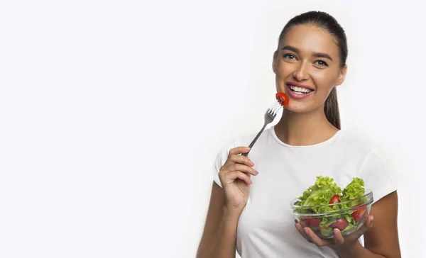 Glad ung kvinna äter sallad stående över vit bakgrund — Stockfoto