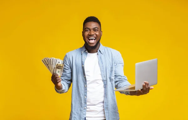 Nadšení černošky chlap drží hotovost a notebook přes žluté pozadí — Stock fotografie
