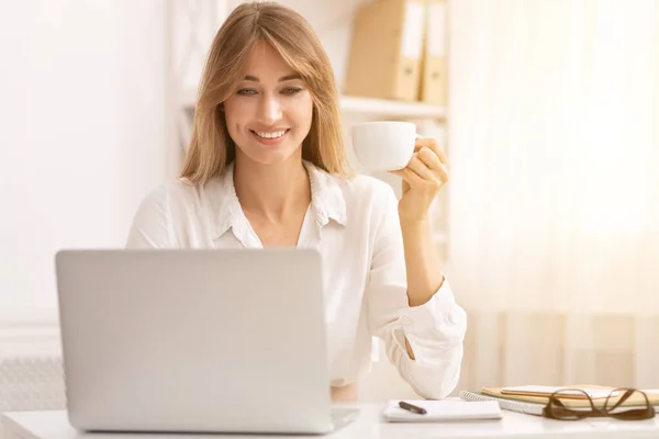 Sonriente chica de la oficina tomando café relajante en el lugar de trabajo — Foto de Stock