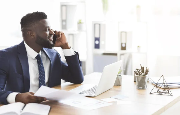 Glimlachende zwarte zakenman checkt rapporten, telefoneert met assistent — Stockfoto