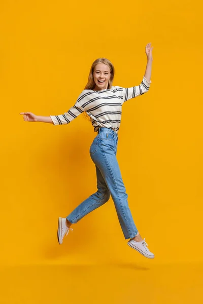 Grappig tiener meisje lopen op lucht springen over oranje achtergrond — Stockfoto