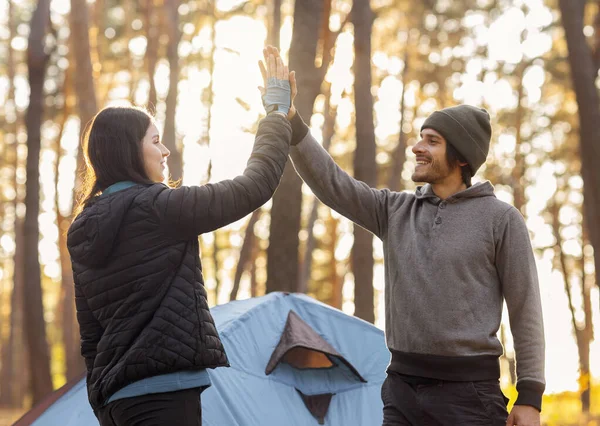 Guy giving girl high five, camping in autumn forest