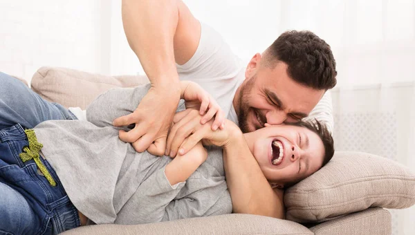 Playful dad tickling his laughing son, laughing on couch together — Stock Photo, Image