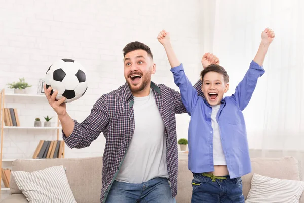 Emocional papá e hijo animando con pelota de fútbol, celebrando gol en casa — Foto de Stock