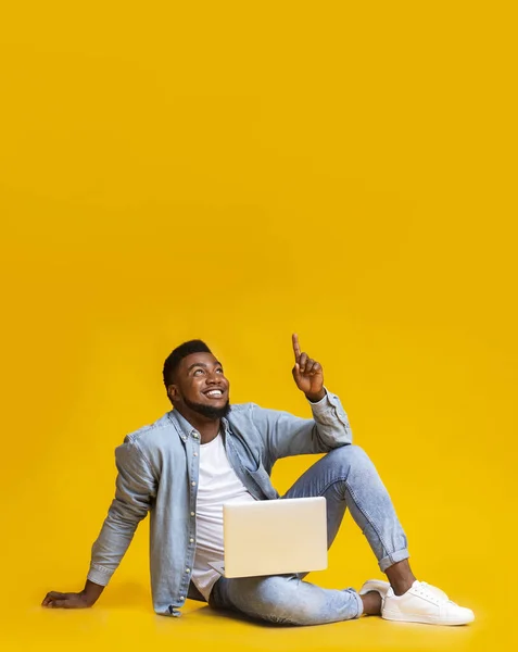 Czarny facet siedzi z laptopem i wskazuje na przestrzeń do kopiowania — Zdjęcie stockowe