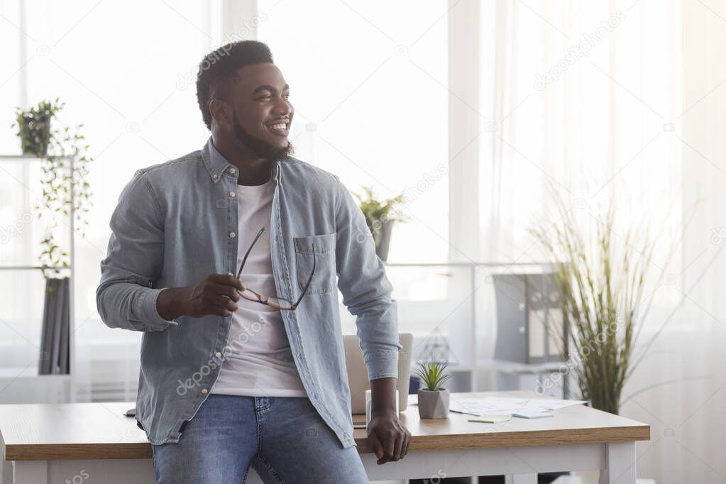 Happy startup owner leaning on office desk and looking aside