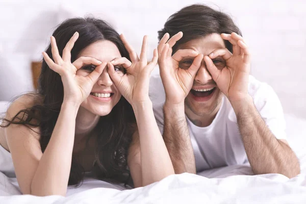 Casal alegre segurando os dedos perto dos olhos como óculos — Fotografia de Stock