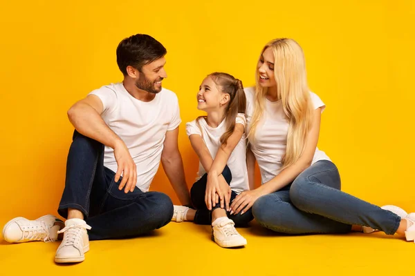 Kochający rodzina rozmowa siedzący na podłodze, żółty tło, Studio strzał — Zdjęcie stockowe