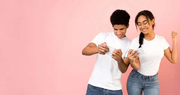 Joyful youngsters playing on smartphones, pink background — Stock Photo, Image