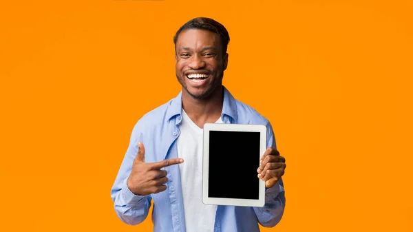 Chico negro señalando el dedo en la pantalla vacía de la tableta, fondo naranja —  Fotos de Stock