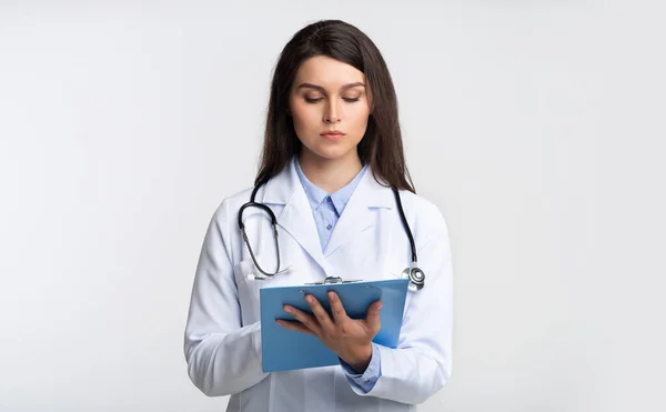 Doctor Lady Reading Informe médico de pie en el fondo del estudio gris —  Fotos de Stock