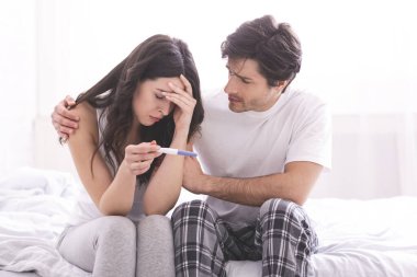 Upset man comforting his depressed wife with negative pregnancy test clipart