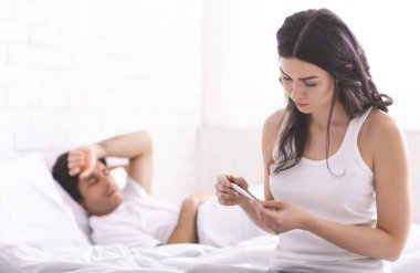 Bakıcı kadın hasta kocasının ateşini ölçüyor.