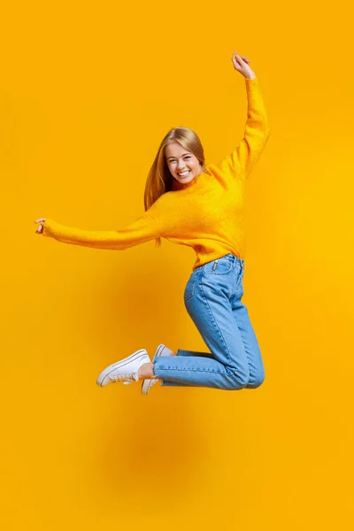 Радостная девочка-подросток, прыгающая в воздух на оранжевом фоне — стоковое фото