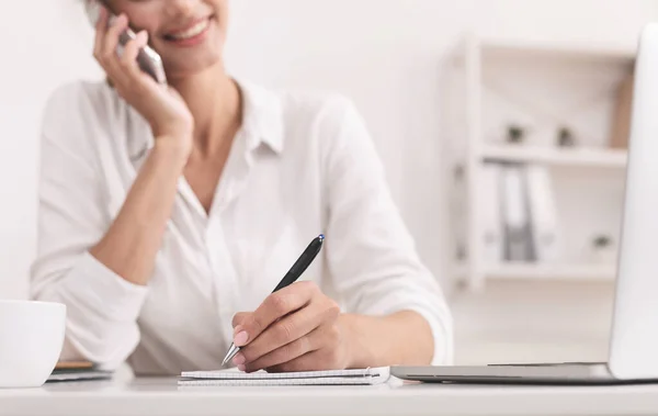 Неузнаваемая деловая женщина, разговаривающая по мобильному телефону, делает заметки в офисе — стоковое фото