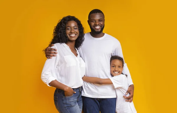 Linda família afro-americana com filha abraçando em fundo amarelo — Fotografia de Stock