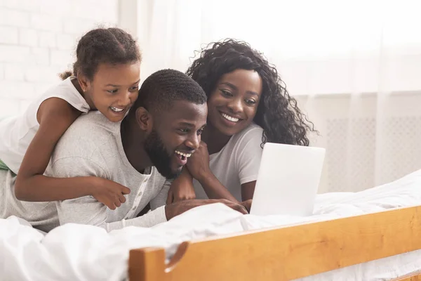 Африканская семья лежит на кровати просматривает интернет на ноутбуке вместе — стоковое фото