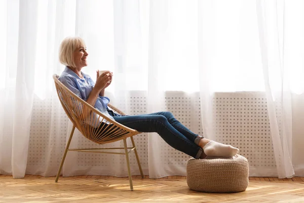 Glückliche Seniorin entspannt sich auf Stuhl am Fenster — Stockfoto