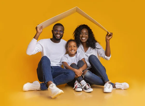 Schwarze Familie sitzt unter symbolischem Dach und träumt von einer neuen Heimat. — Stockfoto