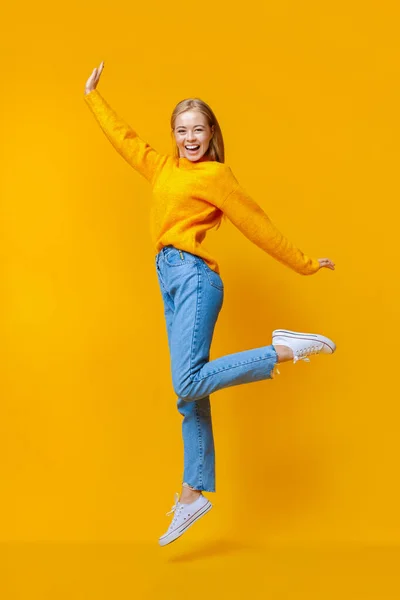 Красива дівчина стрибає в повітрі і сміється на помаранчевому фоні — стокове фото