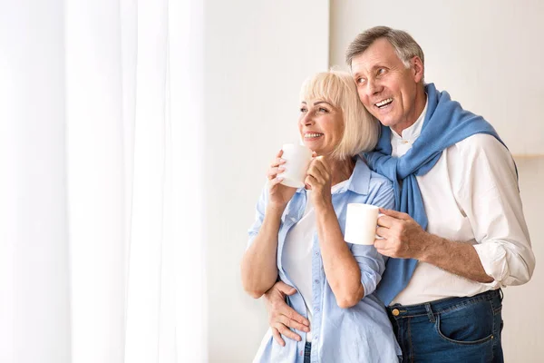 Liebendes Senioren-Paar steht am Fenster und trinkt Tee — Stockfoto