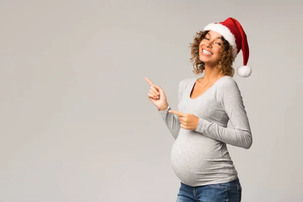 Afro pregnant woman in santa hat pointing at copy space — Stock Photo, Image