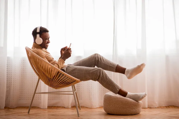 Afro-Typ mit Kopfhörer und Smartphone auf Stuhl im Innenraum — Stockfoto