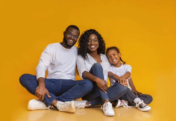 Sonriente familia africana sentada en el suelo sobre fondo amarillo del estudio — Foto de Stock