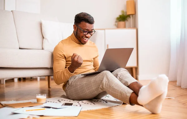 Emocionado negro chico usando portátil sacudiendo puños sentado en casa — Foto de Stock