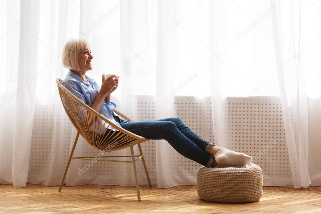 Happy senior woman relaxing on chair near window