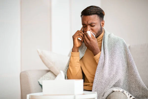 Afro Kerl pustet Nase in Serviette sitzt auf Sofa drinnen — Stockfoto