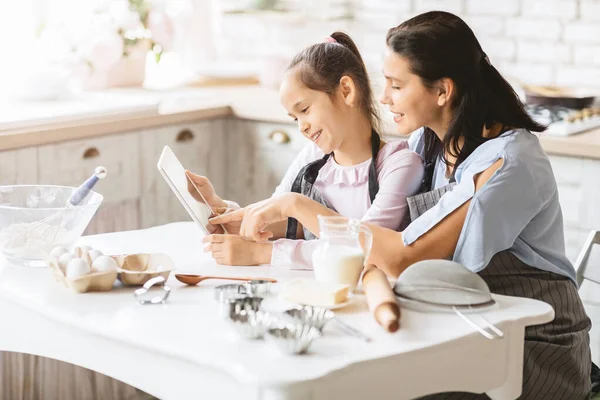 Madre e hija sosteniendo la tableta digital comprobando la receta de masa —  Fotos de Stock