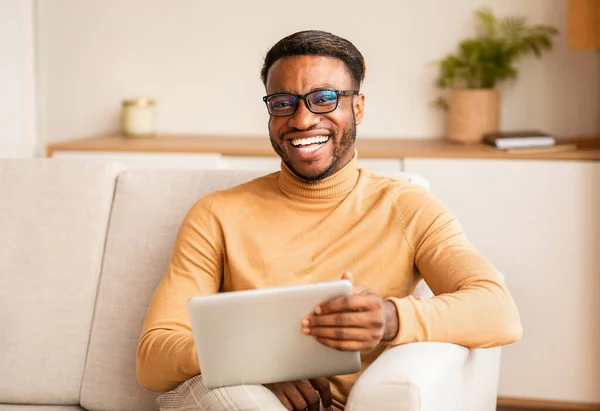 Afro Man Holding Digital Tablet Sitting On Couch At Home