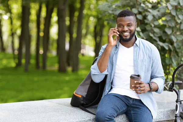Bonito cara preto falando ao telefone enquanto bebe café ao ar livre — Fotografia de Stock