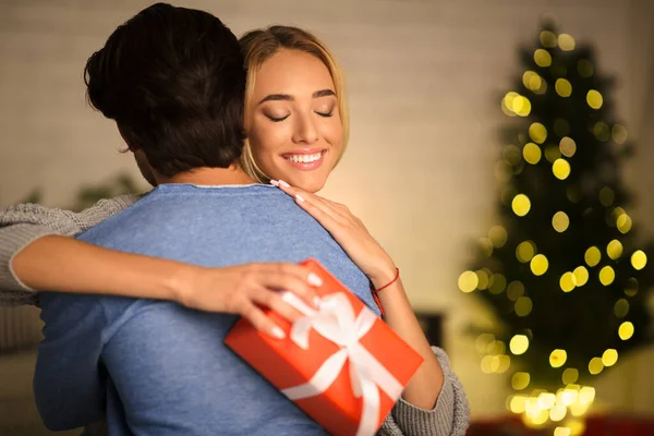 Frohe Weihnachten. dankbare Frau mit Geschenk umarmt Ehemann — Stockfoto