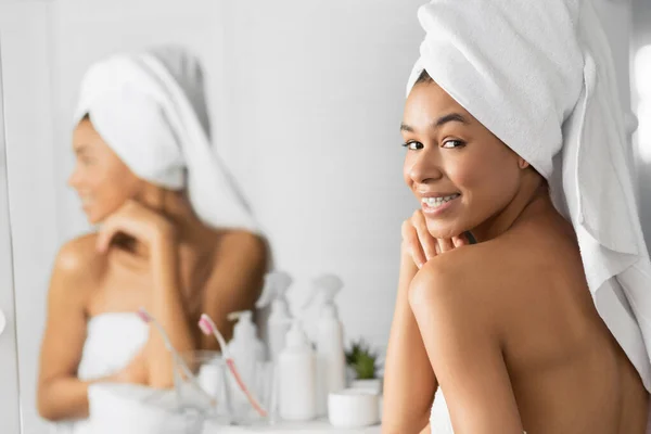 Meisje verpakt in handdoek glimlachen op camera staande in badkamer — Stockfoto