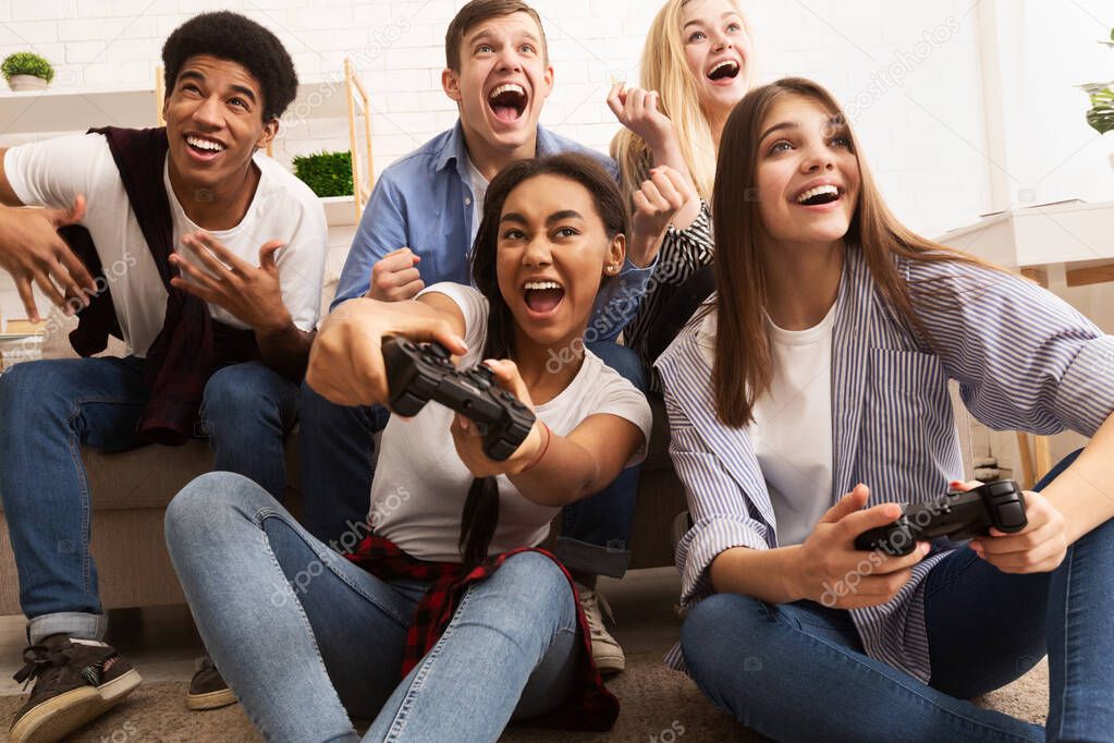 Overjoyed teen friends playing video games at home